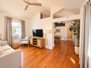 Een ruime woonkamer met een flatscreen televisie, een plafondventilator en een eethoek met een tafel en stoelen.