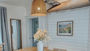 A dining area with a wooden table, wicker pendant light, and a vase of flowers.