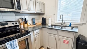 A modern kitchen with stainless steel appliances, white cabinetry, and a wooden floor.