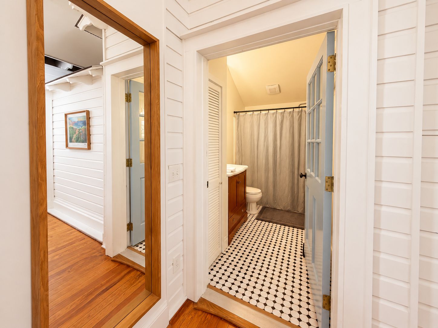 A hallway with a wooden floor leading to a bathroom with a toilet, sink, and shower curtain.