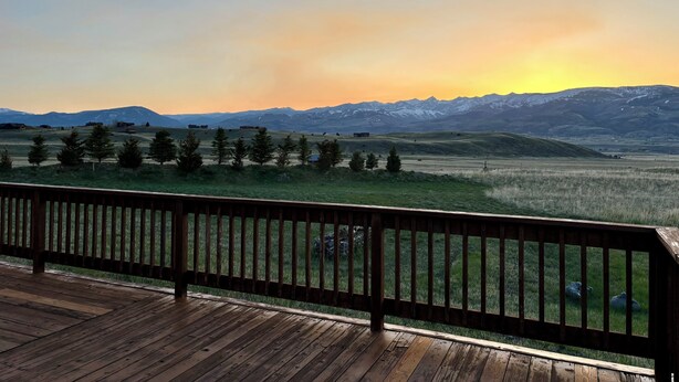 Eine Holzterrasse mit Blick auf eine Berglandschaft im Sonnenuntergang.