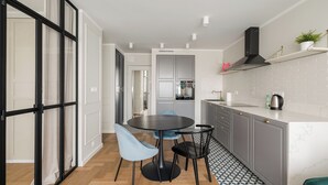 A modern kitchen with a round table and two chairs, a built-in oven, and a countertop with a kettle. - Metro Wierzbno Deluxe Apartment (Warszawa)