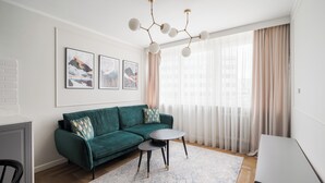 A modern living room with a teal sofa, a round coffee table, and a chandelier. - Metro Wierzbno Deluxe Apartment (Warszawa)