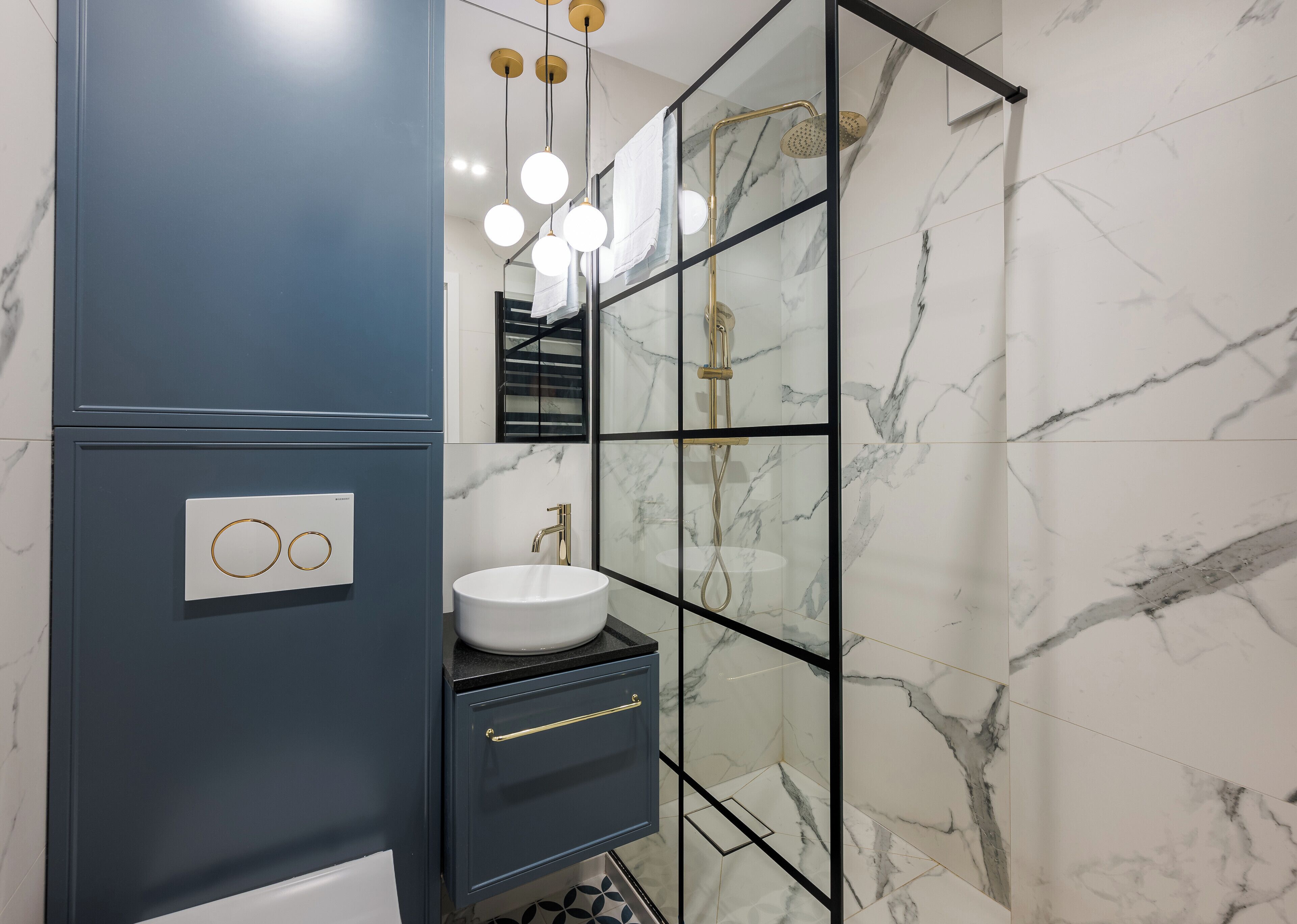 A modern bathroom with a marble-tiled wall, a glass-enclosed shower, and a built-in sink with a gold faucet.