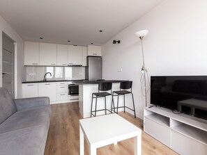 Enjoy a spacious living area with a comfortable sofa, flat-screen TV, and modern kitchen with oven and refrigerator.
