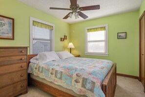 A bedroom with a bed, dresser, ceiling fan, windows with blinds, and a lamp. - Kill Devil Hills 425: Oceanside, Pet Friendly, Hot Tub, Close to Beach Access (Kill Devil Hills)