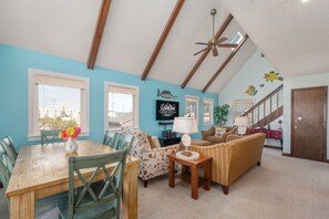 A spacious living room with a high ceiling, a dining area with a wooden table and chairs, and a cozy seating area with a sofa and armchairs. - Kill Devil Hills 425: Oceanside, Pet Friendly, Hot Tub, Close to Beach Access (Kill Devil Hills)