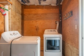 A compact laundry room with a washing machine and dryer, wooden walls, and a visible water pipe.