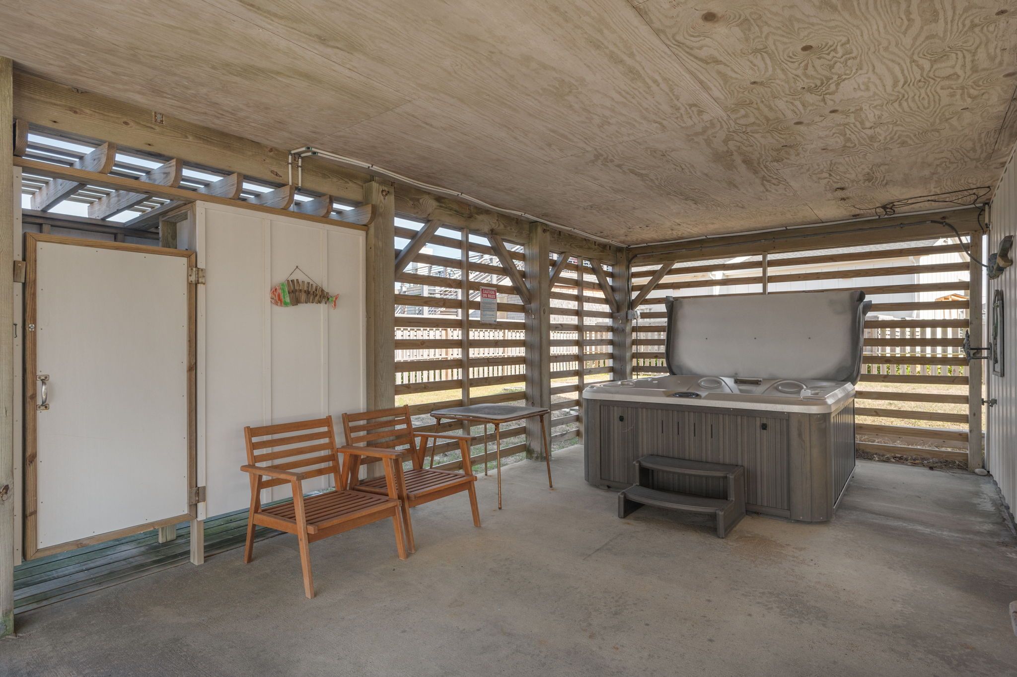 A covered outdoor area with a hot tub, wooden benches, and a wooden fence.