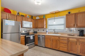 A kitchen with wooden cabinets, stainless steel appliances, a microwave, a sink, and a window with blinds. - Kill Devil Hills 425: Oceanside, Pet Friendly, Hot Tub, Close to Beach Access (Kill Devil Hills)