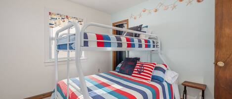 Ein Etagenbett mit gestreifter Bettdecke, ein kleiner Holzschemel und eine Wanddekoration mit Sternen und Muscheln.
