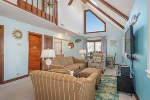 A cozy living room with striped sofas, a wooden ceiling, and a television. - Kill Devil Hills 425: Oceanside, Pet Friendly, Hot Tub, Close to Beach Access (Kill Devil Hills)