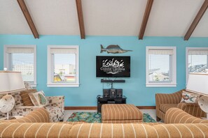 Sala de estar com parede azul, vigas de madeira, televisão na parede e dois sofás.