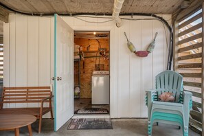 Um interior rústico com um banco de madeira, uma cadeira de plástico verde e uma máquina de lavar nos fundos.