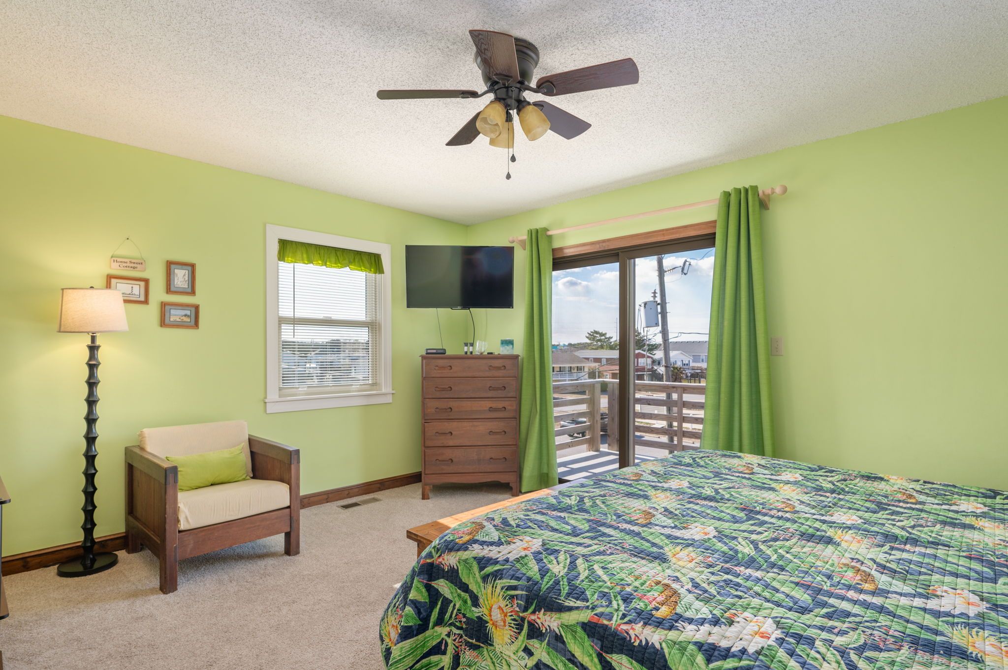 A bedroom with a bed, a chair, a dresser, a TV, and a balcony with a view.