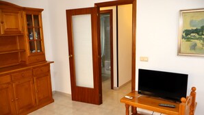 A room with a wooden cabinet, a television on a wooden stand, and a door leading to another room. - Los Pescadores playa LEK (Peñiscola)