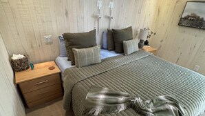 Een slaapkamer met een bed, nachtkastjes, een lamp en een wandplank.