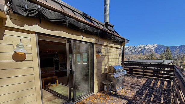 Een houten gebouw met een schuifdeur, een barbecue en uitzicht op besneeuwde bergen.