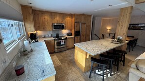 Een moderne keuken met houten kastjes, roestvrijstalen apparatuur, een granieten aanrechtblad en een centraal eiland met barstoelen.