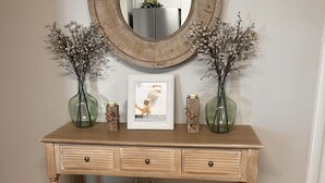 Un tavolo consolle in legno con uno specchio, due vasi con fiori secchi, un quadro incorniciato e un cesto di vimini.