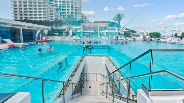 Ein großer, überdachter Pool mit klarem, blauem Wasser, umgeben von Liegestühlen und Sonnenschirmen.