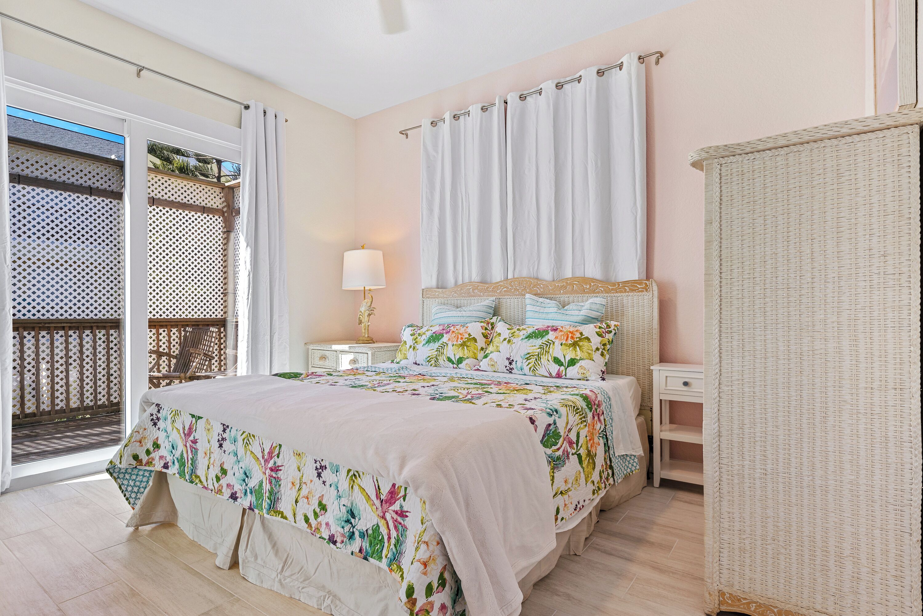 Une chambre à coucher avec un lit, une table de chevet, un fauteuil en osier et une vue sur l’extérieur.