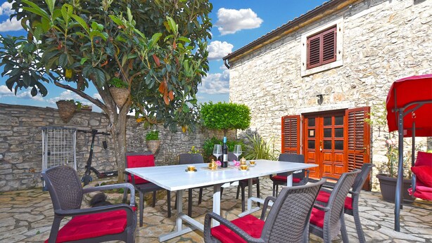An outdoor patio with a stone wall, wicker furniture, and red cushions.