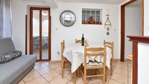 A dining area with a table set for two, a wooden chair, a sofa, and a large wall clock.