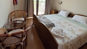 Ein Hotelzimmer mit einem Bett, einem Glastisch mit Stühlen, einem Bild an der Wand und einem Fenster mit Vorhängen.