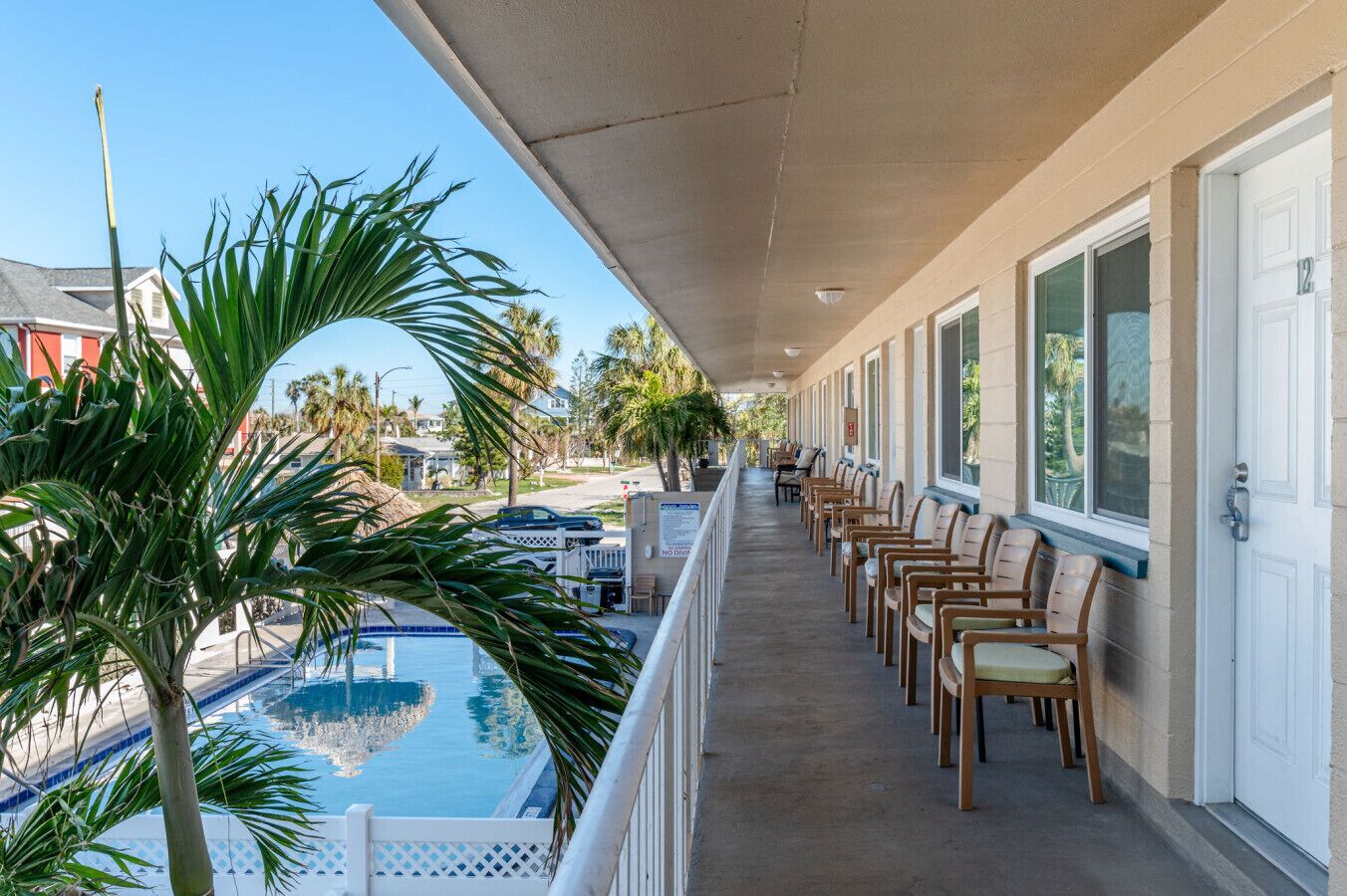 Een hotelbalkon met een zwembad, stoelen en palmbomen.
