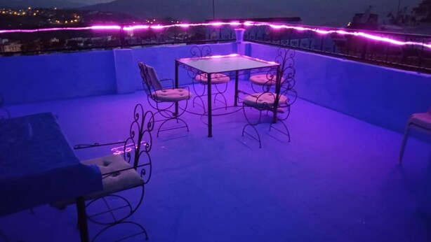 A rooftop terrace with a table and chairs, surrounded by a low wall and a view of the cityscape. - CASA DAOUED APRT B (CHEFCHAOUEN)
