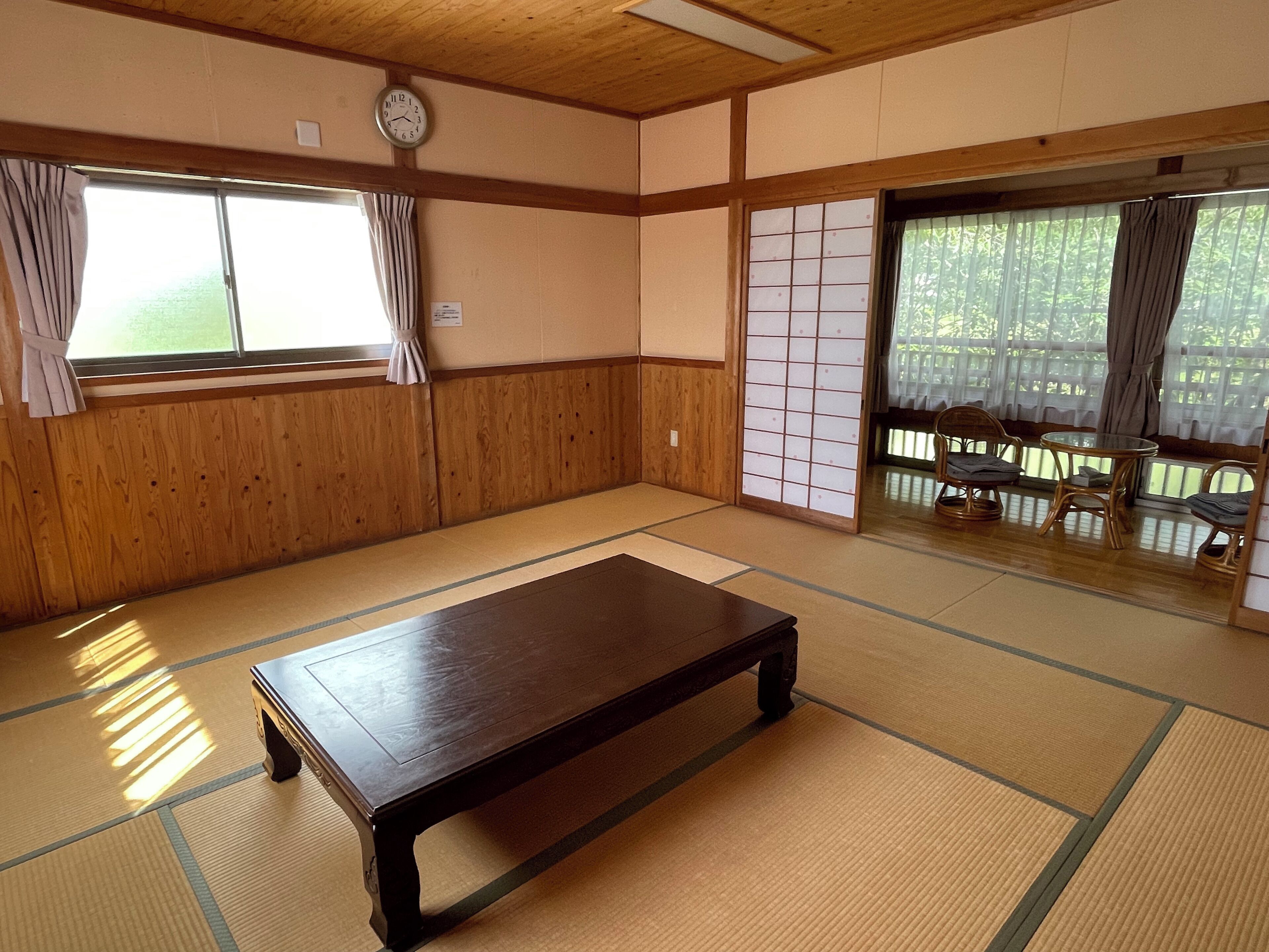 A traditional Japanese room with tatami flooring, a low wooden table, sliding doors, and a view through a window.