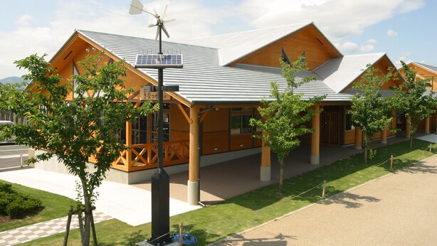 A modern building with a sloped roof, solar panels, and a wind turbine. - kinasse (Yamaga)