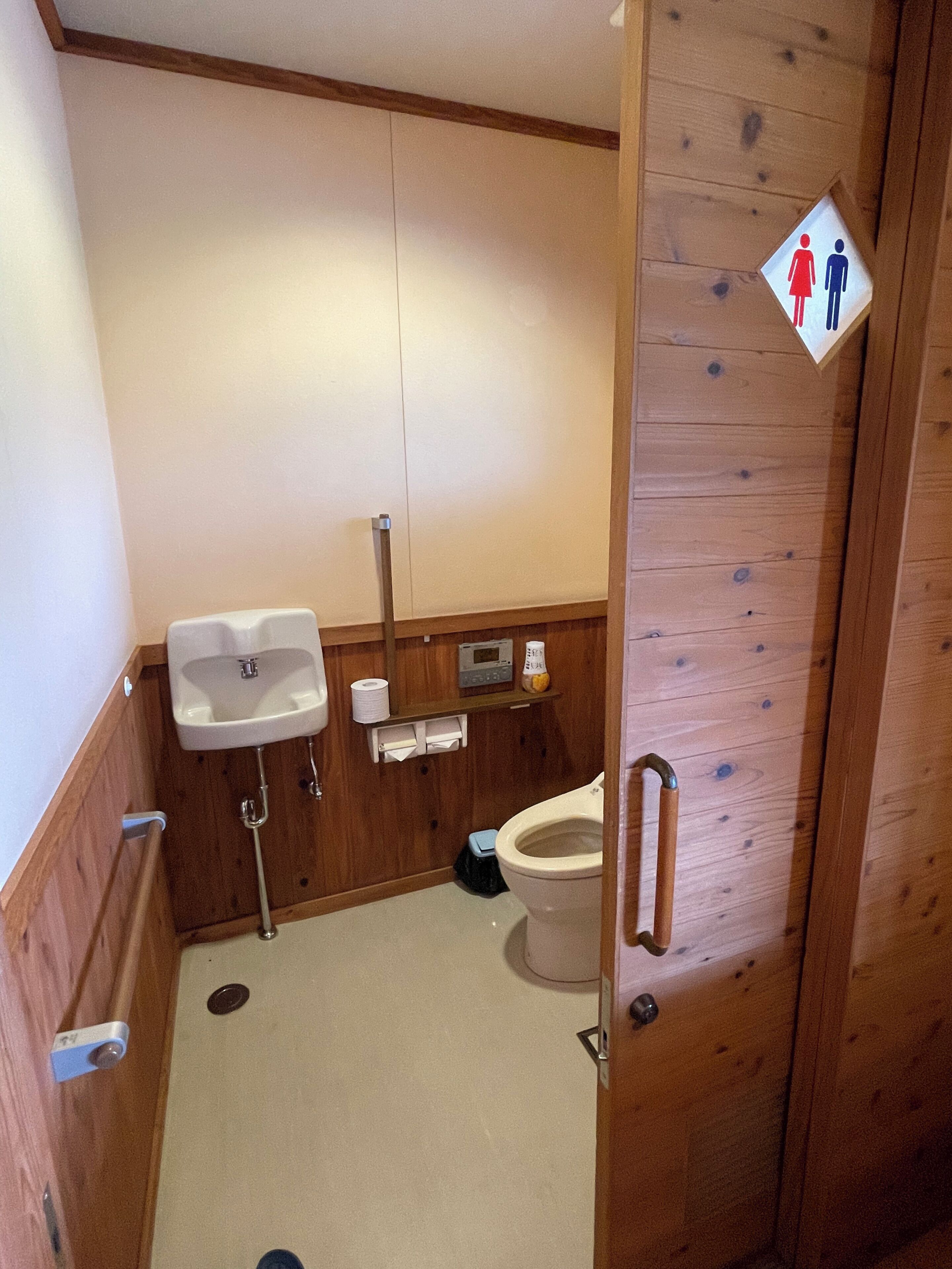 A small, wooden-finished bathroom with a toilet, a sink, and a hand dryer.