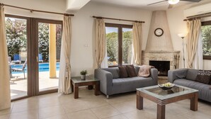 A living room with a sofa, a glass coffee table, a fireplace, and a view of a swimming pool. - Tsikkos Pende awaits you in Argaka, Cyprus (Argaka)