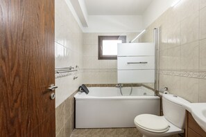 Een badkamer met een bad, toilet en een houten deur.