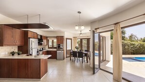 A modern kitchen with a central island, built-in appliances, and a dining area with a view of a swimming pool. - Tsikkos Pende awaits you in Argaka, Cyprus (Argaka)