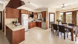 A modern kitchen with wooden cabinets, a central island, a dining area with a table and chairs, and a ceiling fan. - Tsikkos Pende awaits you in Argaka, Cyprus (Argaka)