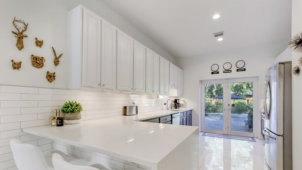 A modern kitchen with white cabinetry, a central island, and a dining area with white chairs. - Tropical Oasis, Heated Pool, Near Las Olas Beach (Fort Lauderdale)