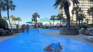 A blue pool area with palm trees and a building in the background.