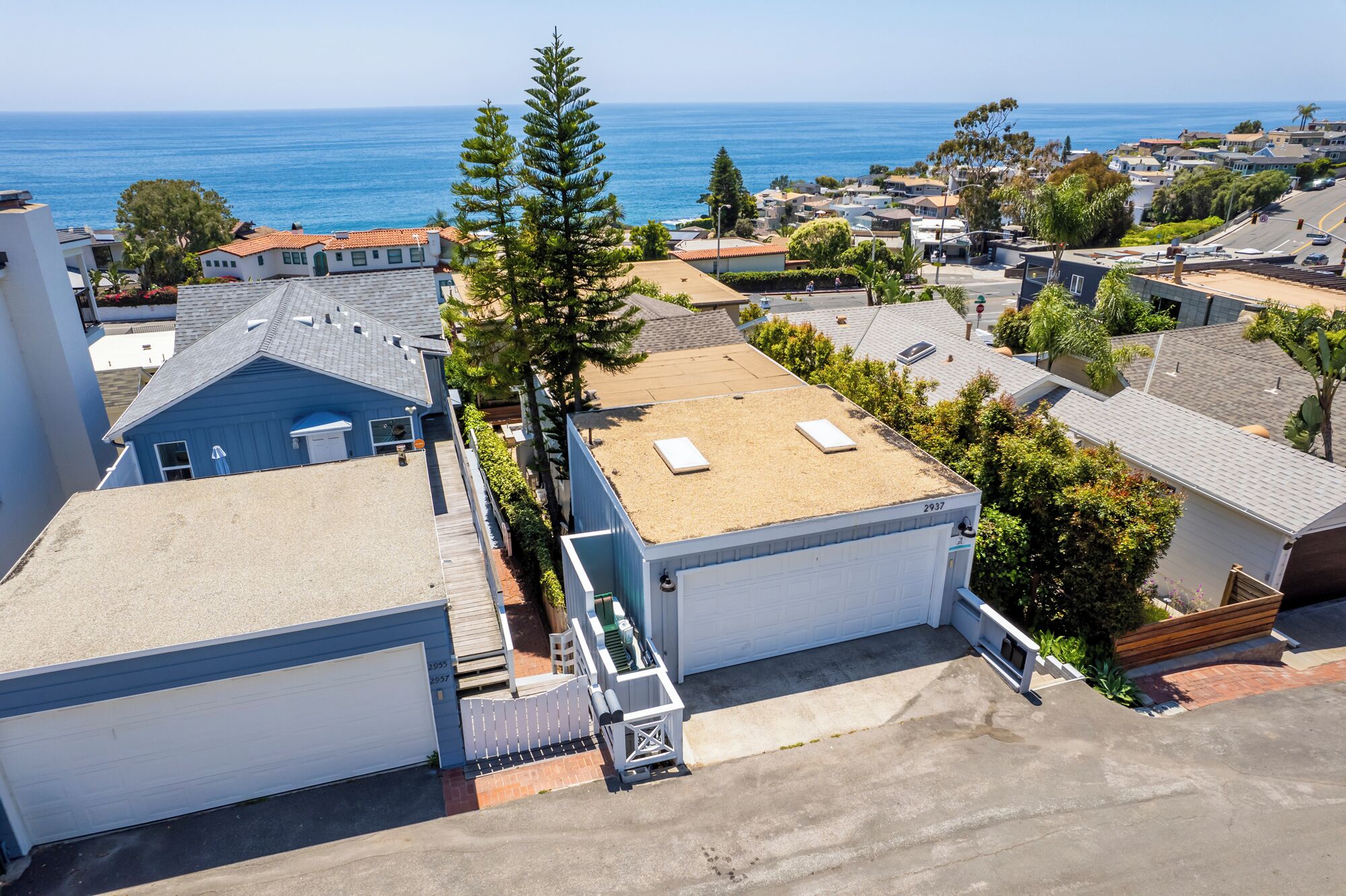 A residential area with a clear view of the ocean, houses with sloped roofs, and a prominent tree.