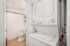 Ein kleines, modernes Badezimmer mit Toilette, Duschvorhang und integrierter Waschmaschine und Trockner.