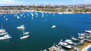 A marina with numerous boats docked, a cityscape in the background, and a clear blue sky. - Gorgeous and Modern Duplex near the Beach! (Newport Beach)