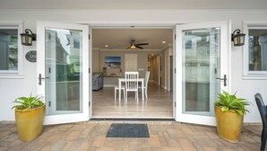 Una entrada moderna con puertas de cristal, un comedor con mobiliario blanco y plantas en macetas.