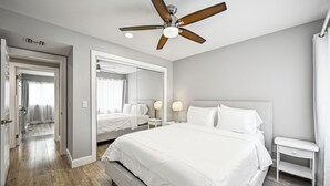 Un dormitorio moderno con una cama grande, un ventilador de techo, una mesita de noche y un espejo.