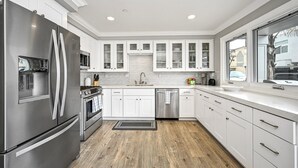 Una cocina moderna con electrodomésticos de acero inoxidable, armarios blancos y un amplio ventanal con vistas al exterior.