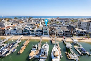 A marina with multiple boats docked, surrounded by residential buildings and a beach in the background.