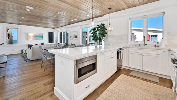 A modern kitchen with white cabinetry, a central island, stainless steel appliances, and pendant lighting.