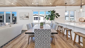 A modern kitchen with a white countertop, wooden stools, and a hanging light fixture.