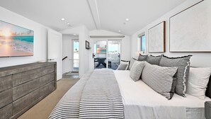 A bedroom with a bed, a wooden dresser, and a large painting of a beach scene.
